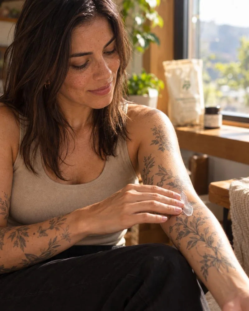 Mujer tatuada aplicándose una capa fina de crema en el antebrazo, con la bolsa Dermatinta al fondo (imagen creada con IA).